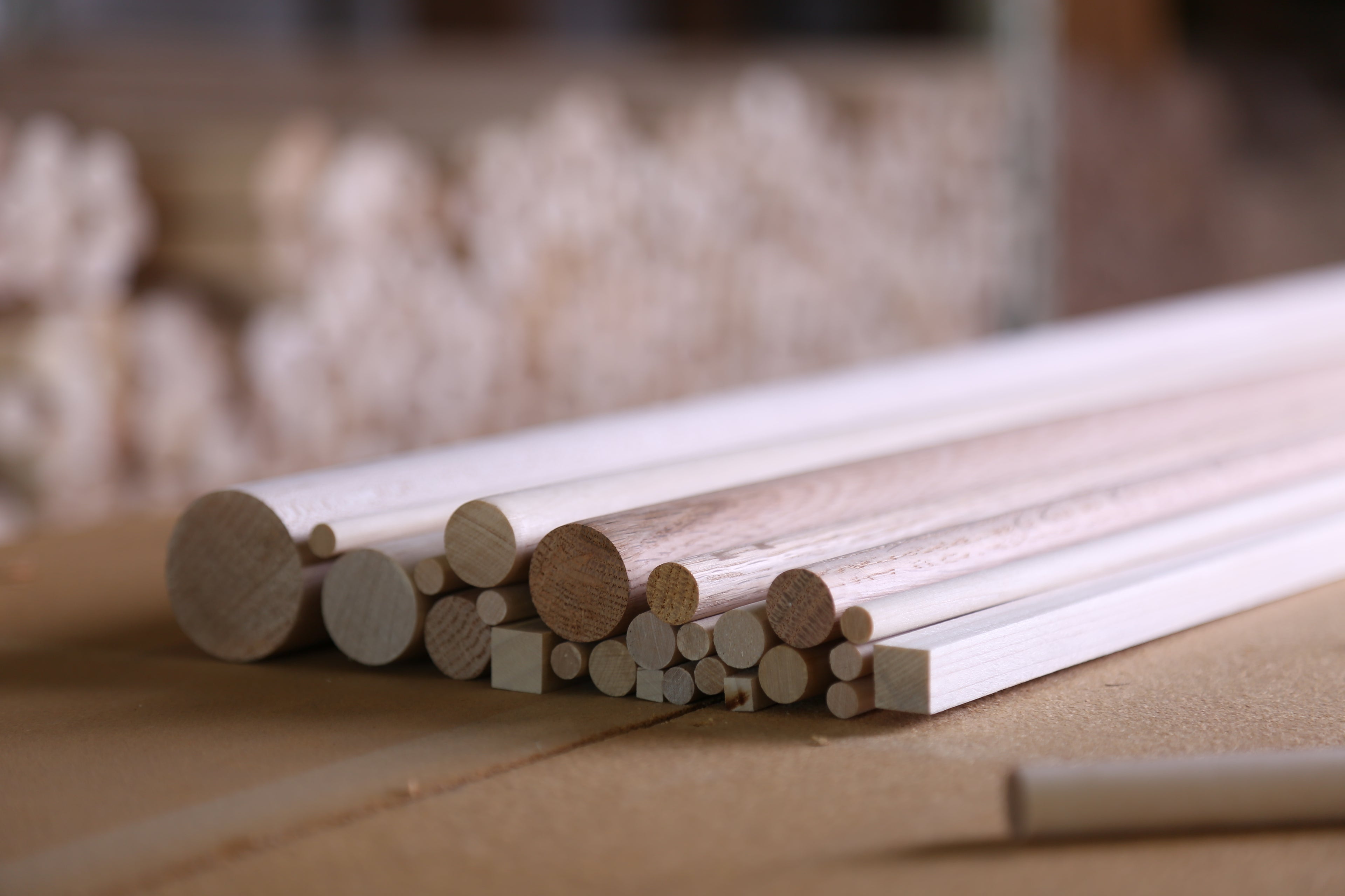 Assorted unfinished wood dowels and square dowel rods arranged on a wooden work surface